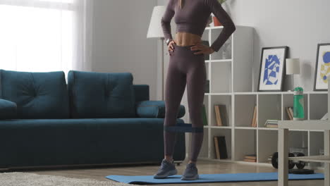 fitness-elastic-band-for-physical-exercise-woman-is-using-it-for-legs-moving-leg-to-side-tensing-muscles-home-workout-view-on-slender-body